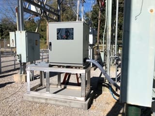 Outdoor electrical control panel mounted on a metal frame under sunlight.